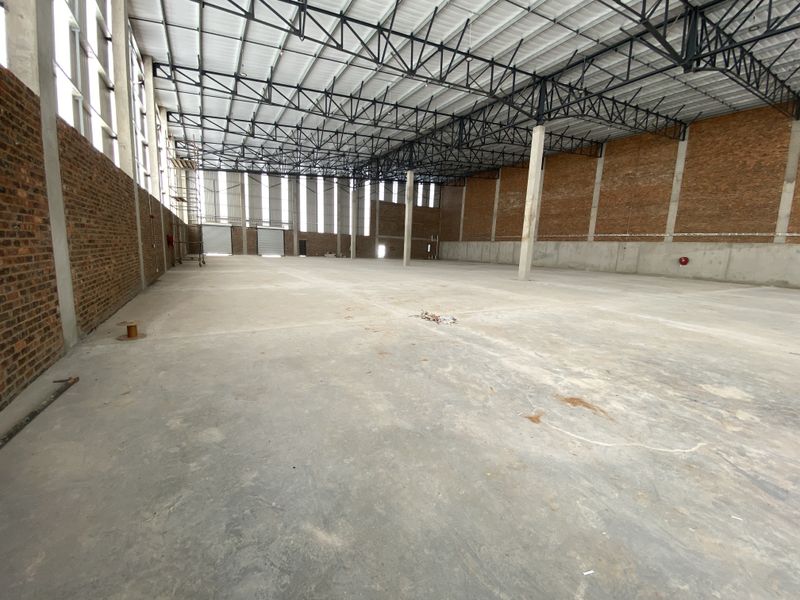 Spacious industrial warehouse featuring high ceilings with exposed steel trusses, concrete flooring, and large roller shutter doors for efficient access.