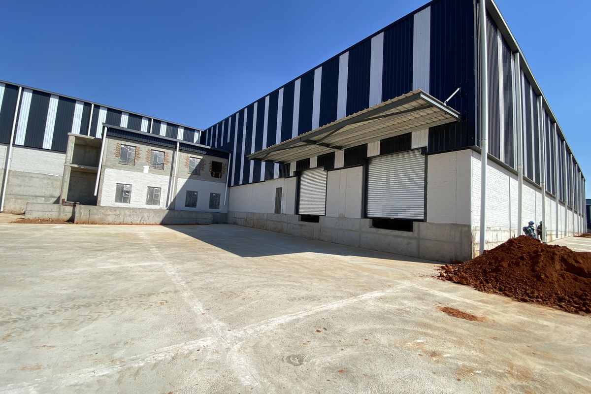 Industrial warehouse exterior featuring a large concrete yard, metal cladding, and multiple roller shutter loading doors under a canopy.
