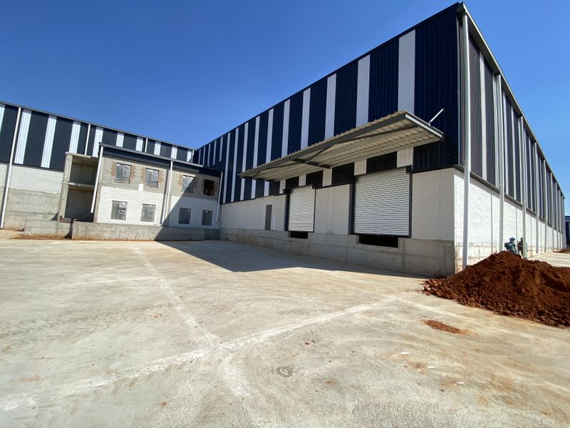 Industrial warehouse exterior featuring a large concrete yard, metal cladding, and multiple roller shutter loading doors under a canopy.