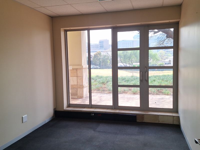 An empty office space featuring a suspended ceiling, recessed lighting, carpeted flooring, and a glass door providing access to an outdoor patio area.