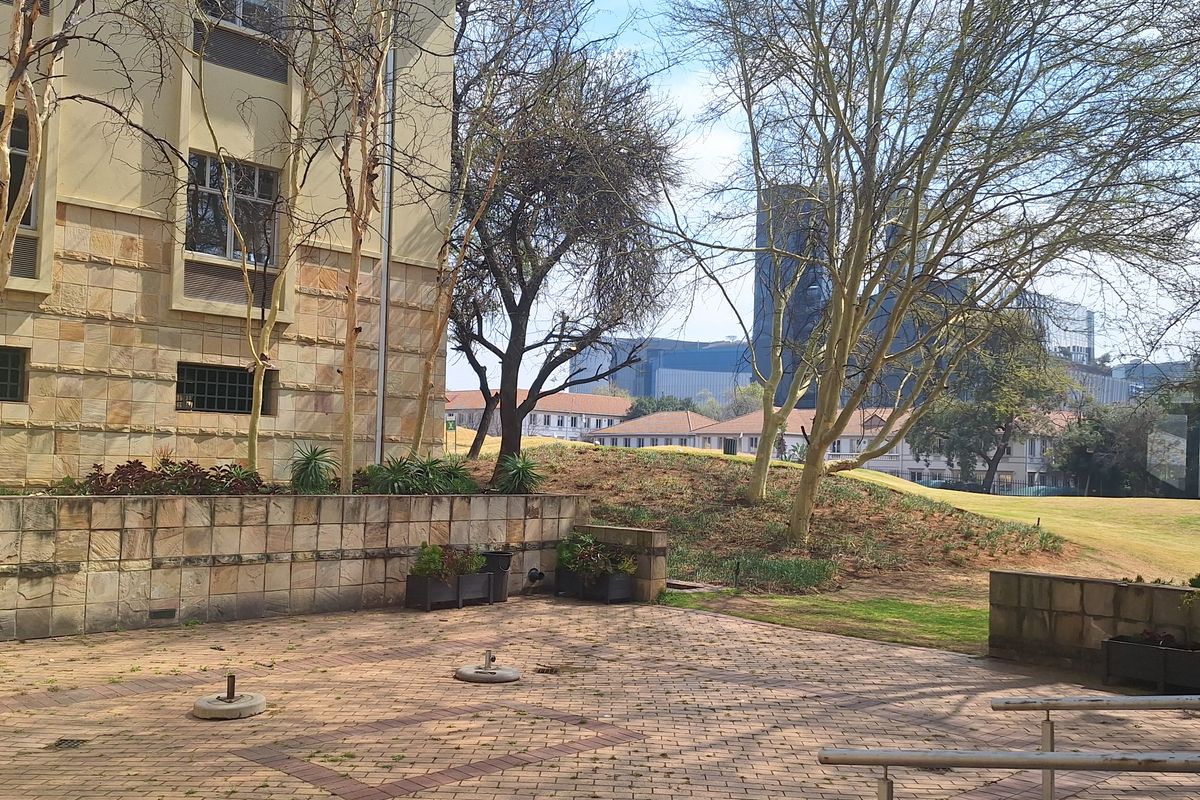 Rear exterior courtyard featuring stone-clad building facade, paved ground surface, and metal handrails, overlooking a landscaped garden area.