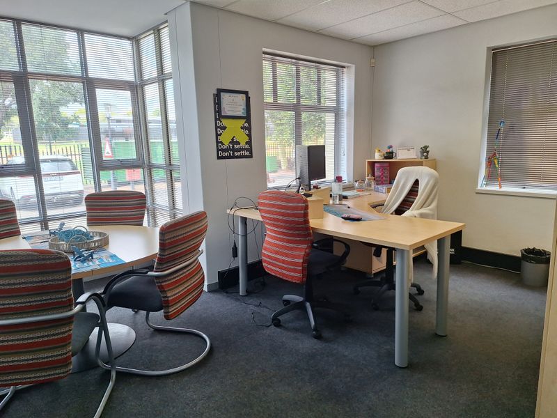 A bright, functional office space featuring large windows with venetian blinds, carpeted flooring, and a suspended ceiling, suitable for professional use.
