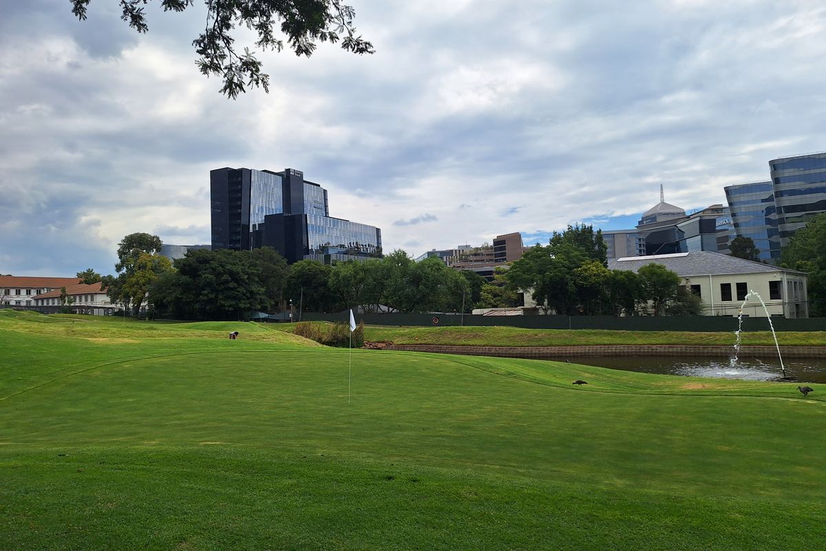 A scenic view overlooking a well-maintained golf course with a water feature and surrounding urban office buildings in the background.