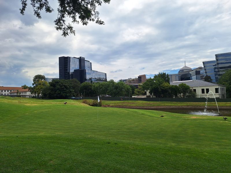 A scenic view overlooking a well-maintained golf course with a water feature and surrounding urban office buildings in the background.