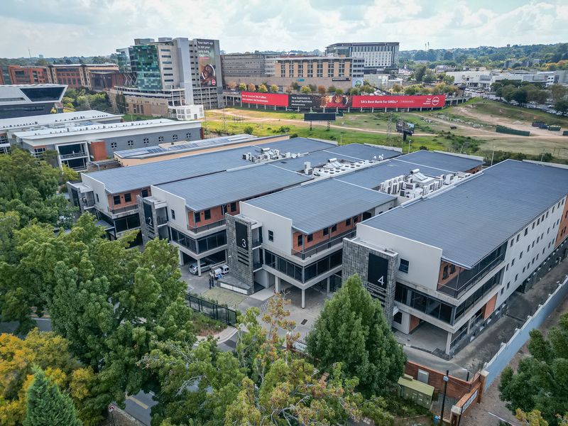 Aerial view of a modern multi-story office complex featuring metal roofing, integrated HVAC systems, and private balconies within a landscaped business park setting.