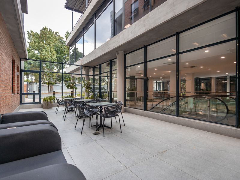 Modern outdoor patio area featuring large glass office facade, concrete flooring, and exposed brickwork, providing a professional and contemporary workspace environment.