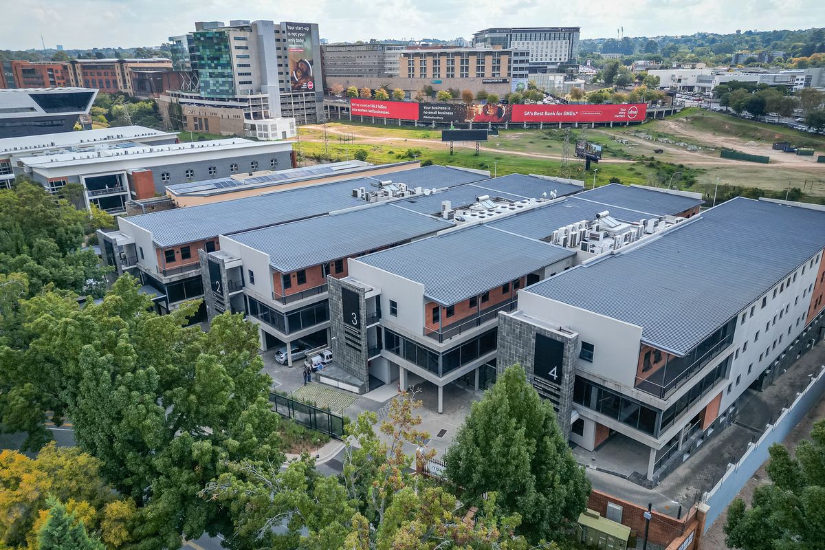 Aerial view of a modern multi-story office complex featuring metal roofing, integrated HVAC systems, and private balconies within a landscaped business park setting.