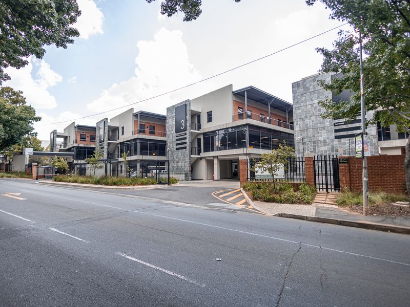 Street view of a modern multi-story office complex featuring stone cladding, glass facades, and secure gated access.