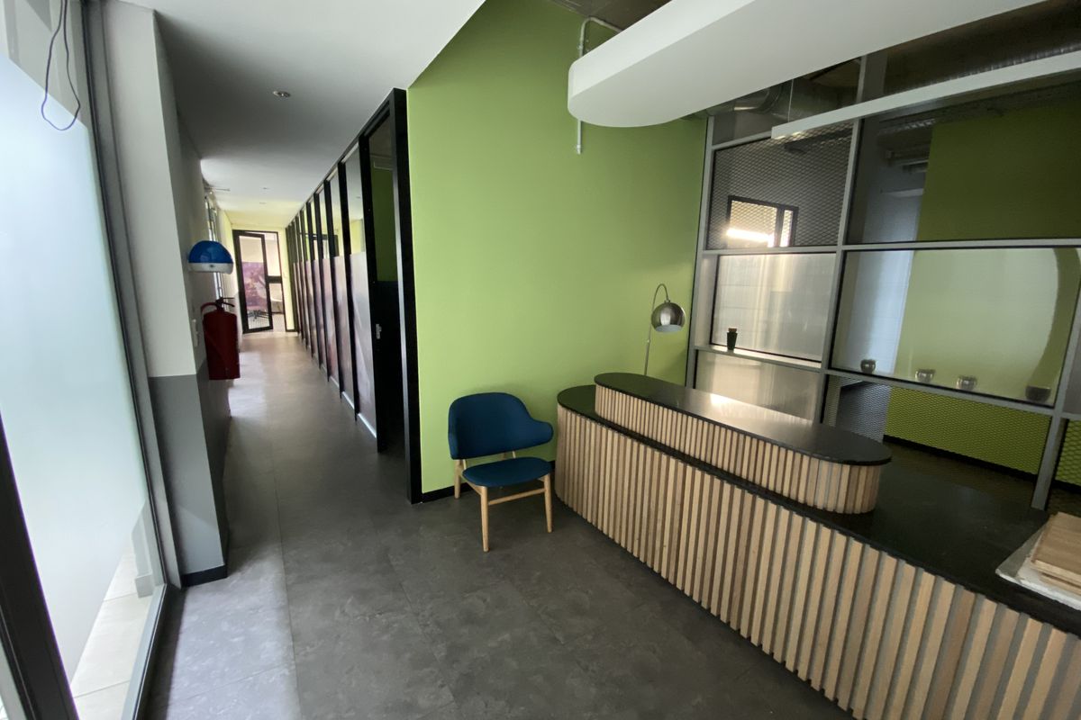 Modern office reception area featuring a custom slatted built-in desk, glass partitions, and vibrant green accent walls with clean tiled flooring.