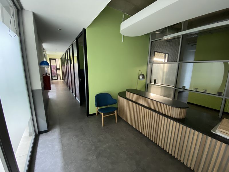 Modern office reception area featuring a custom slatted built-in desk, glass partitions, and vibrant green accent walls with clean tiled flooring.