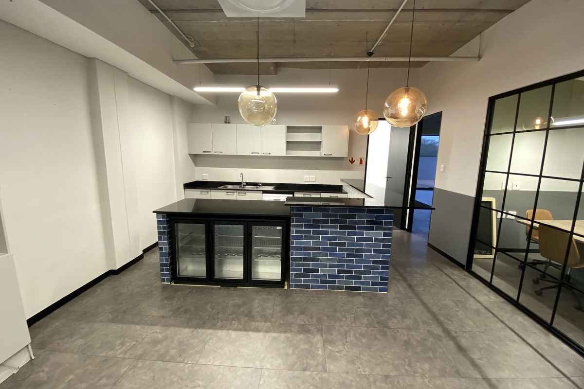 Modern office kitchenette featuring a tiled island, integrated under-counter refrigeration, sleek cabinetry, and an industrial-style exposed concrete ceiling.