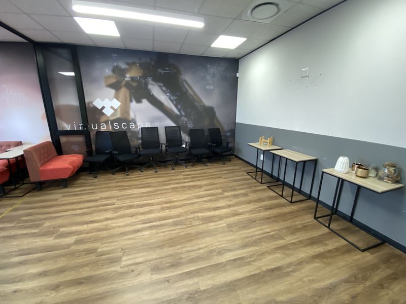 A modern office space featuring laminate flooring, a suspended ceiling with recessed lighting, and a glass partition wall with branded graphic decal.