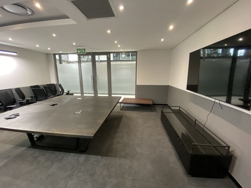 A modern office meeting room featuring recessed lighting, ducted air conditioning, and a glass partition door, providing a professional and functional workspace.