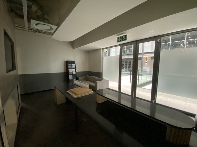 Modern office space featuring a built-in reception desk, exposed industrial ceiling elements, and glass doors leading to an internal building atrium.