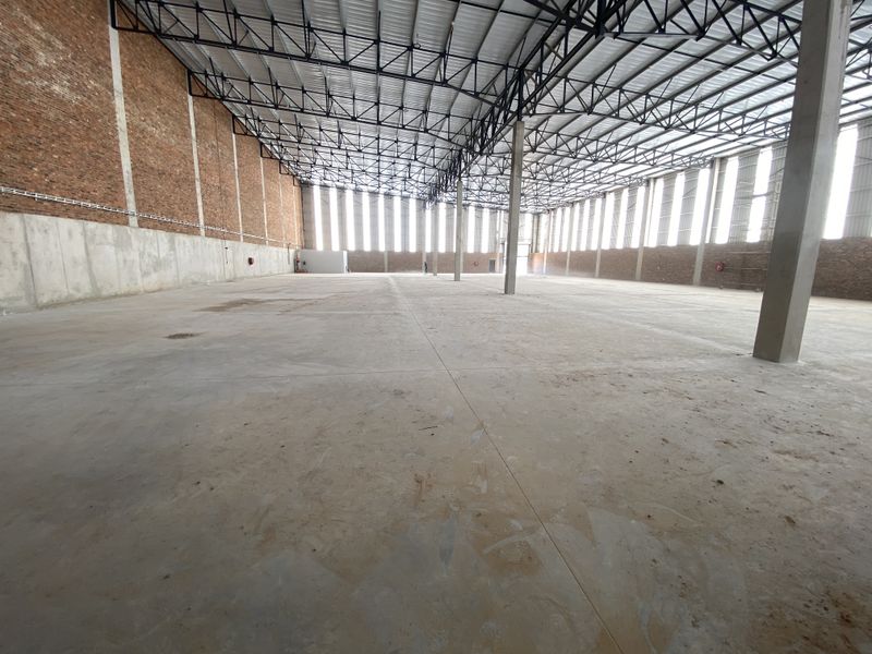 Spacious industrial warehouse interior featuring high ceilings with exposed steel trusses, concrete flooring, and large clerestory windows providing ample natural light.