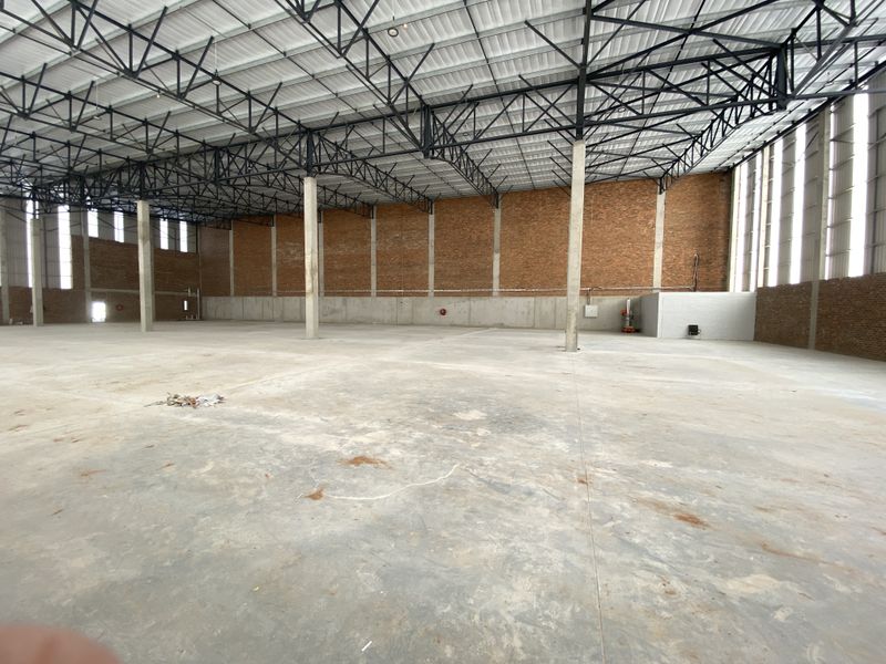 Spacious industrial warehouse featuring high-bay ceilings, exposed steel roof trusses, concrete flooring, and robust brick masonry walls.