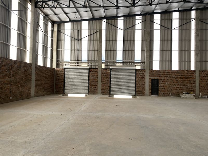 Spacious industrial warehouse unit featuring high ceilings, exposed brickwork, concrete flooring, and dual roller shutter doors for efficient access.