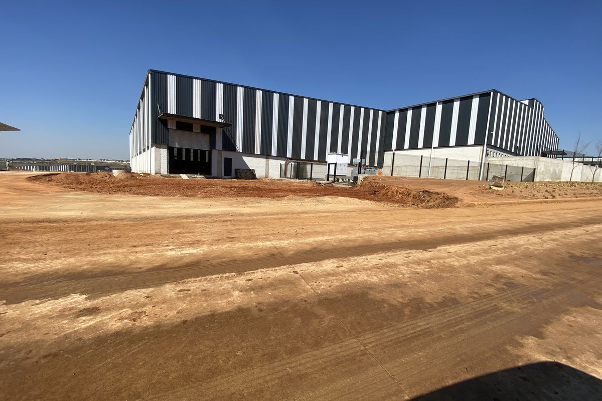 Exterior view of a modern industrial warehouse facility featuring metal cladding, a roller shutter door, and ongoing site development.