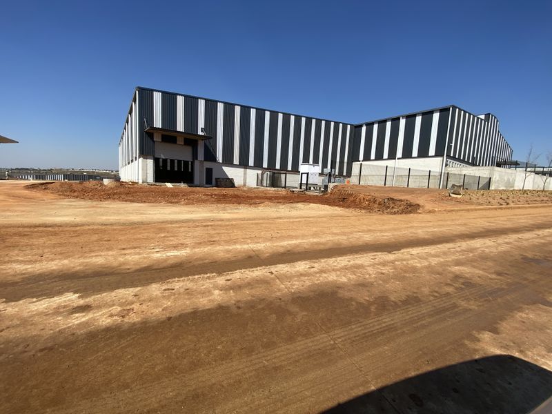 Exterior view of a modern industrial warehouse facility featuring metal cladding, a roller shutter door, and ongoing site development.