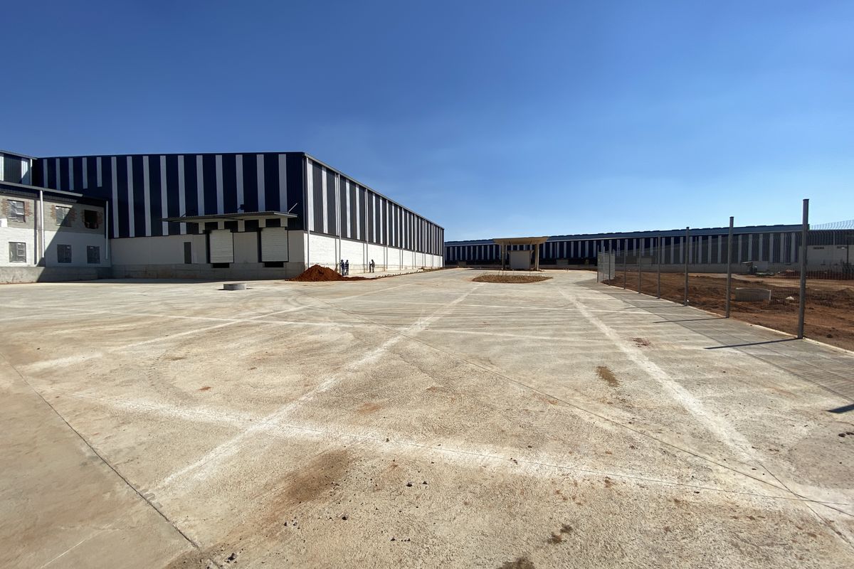 Expansive industrial property featuring a large concrete yard, warehouse structures with loading docks, and perimeter fencing under a clear blue sky.