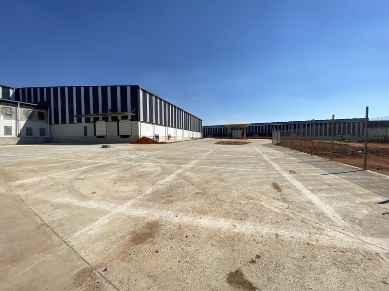 Expansive industrial property featuring a large concrete yard, warehouse structures with loading docks, and perimeter fencing under a clear blue sky.