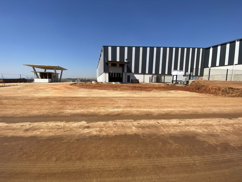 Industrial warehouse facility featuring metal cladding, a roller shutter door, and a separate security gatehouse, set within an expansive, unfinished site.