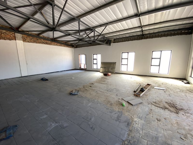 Spacious industrial utility area featuring exposed steel roof trusses, tiled flooring, and large windows, currently in an unfinished state.