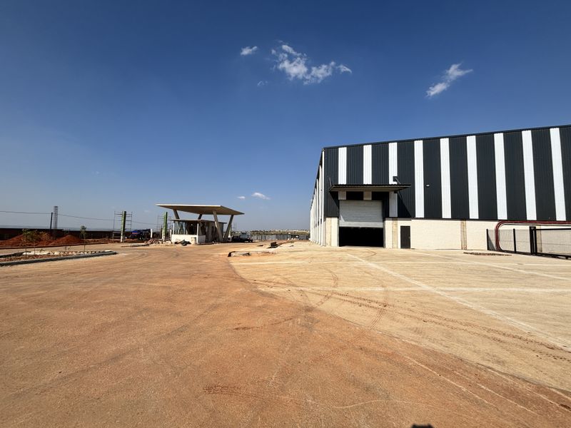 Industrial warehouse facility featuring a large roller shutter door, concrete yard space, and a dedicated security guard house at the entrance.