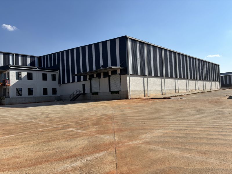 Industrial warehouse facility featuring large metal cladding, roller shutter loading doors, and a spacious concrete yard area.