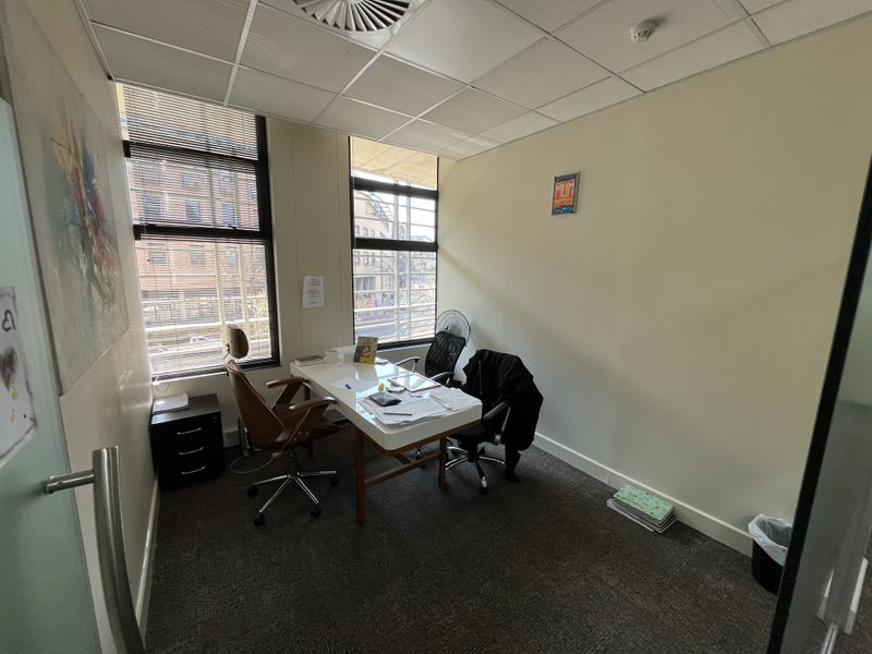 A functional office space featuring a suspended ceiling, large windows with venetian blinds, and carpeted flooring, providing a professional work environment.