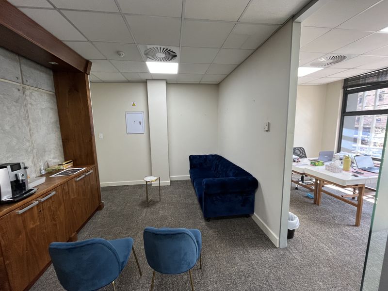 A professional office space featuring built-in wooden cabinetry, carpeted flooring, and a suspended ceiling with recessed lighting, adjacent to a secondary workspace area.