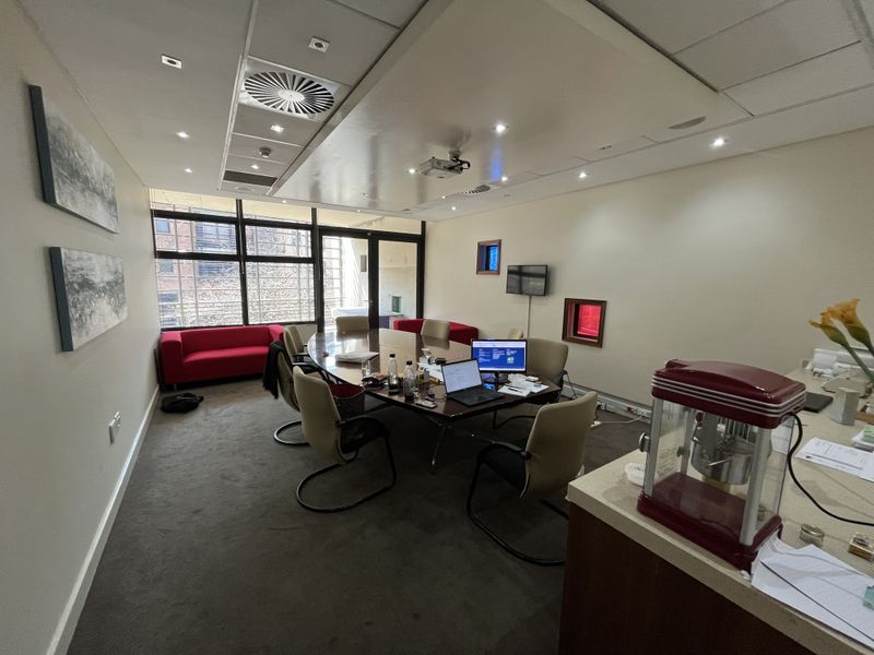 A professional office boardroom featuring recessed ceiling lighting, integrated air conditioning, a ceiling-mounted projector, and large windows providing natural light.