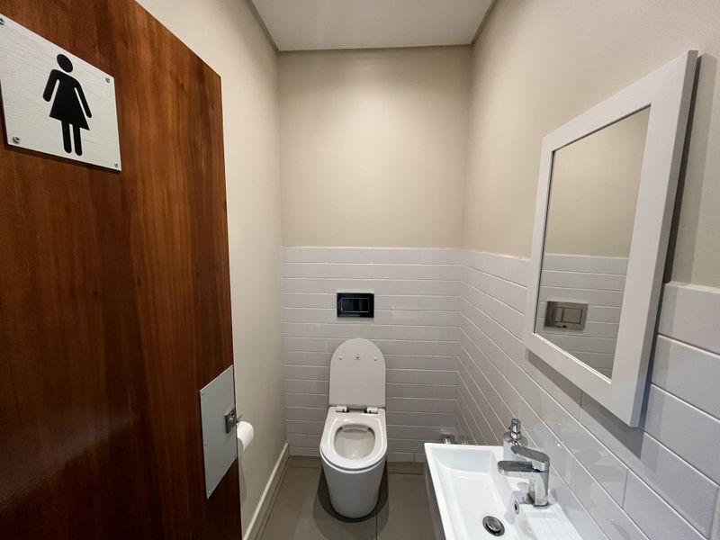 A clean, modern office restroom featuring a wall-mounted toilet, subway tile backsplash, and a sleek wall-mounted basin with chrome fixtures.