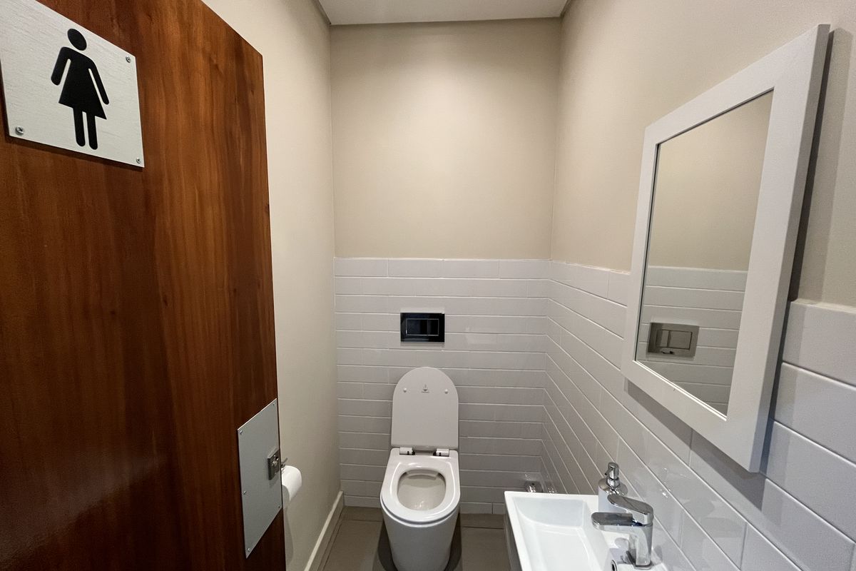 A clean, modern office restroom featuring a wall-mounted toilet, subway tile backsplash, and a sleek wall-mounted basin with chrome fixtures.