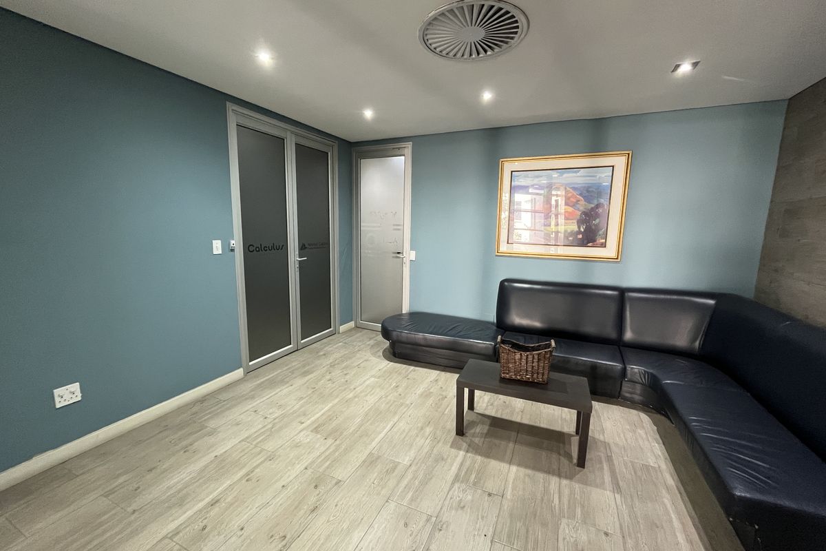 A modern office reception or waiting area featuring wood-look flooring, recessed lighting, and frosted glass doors.