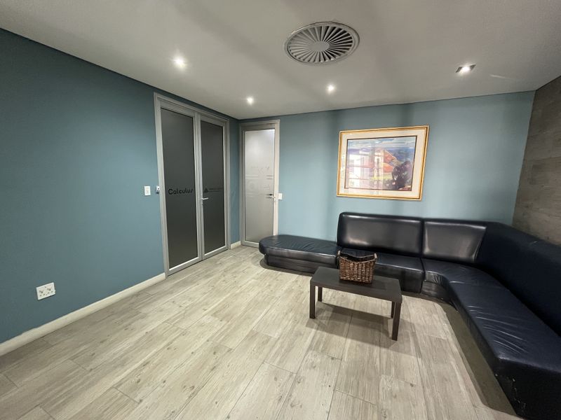 A modern office reception or waiting area featuring wood-look flooring, recessed lighting, and frosted glass doors.