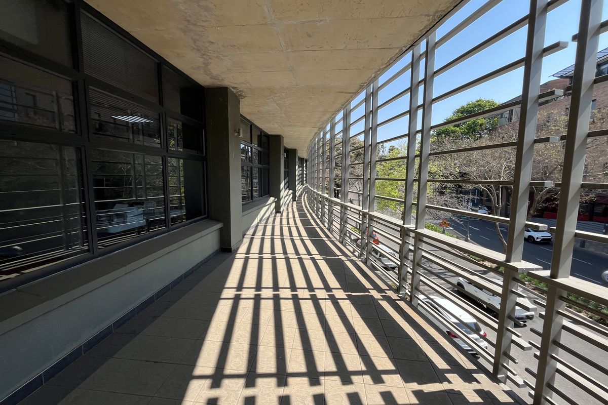 A spacious covered balcony featuring tiled flooring, large glass windows, and a protective metal screen, offering an airy outdoor transition space for the office.