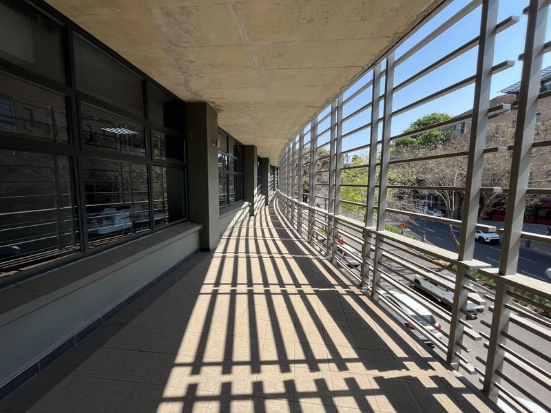 A spacious covered balcony featuring tiled flooring, large glass windows, and a protective metal screen, offering an airy outdoor transition space for the office.