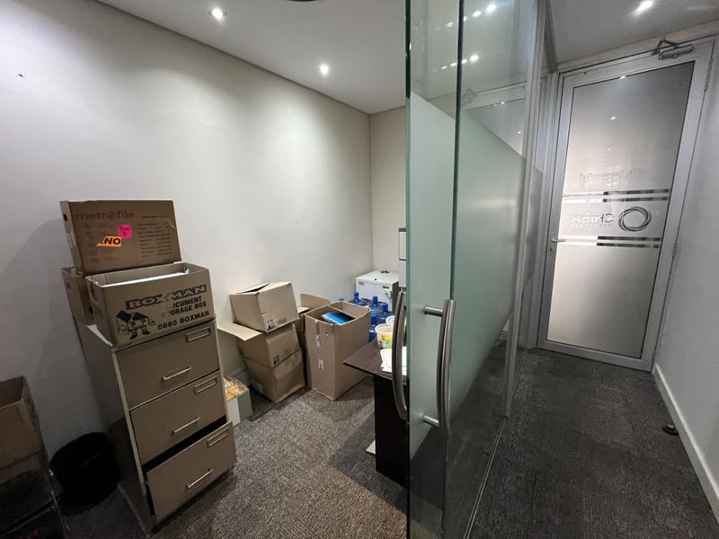 A compact office space featuring a glass partition, frosted glass door, recessed lighting, and carpeted flooring.