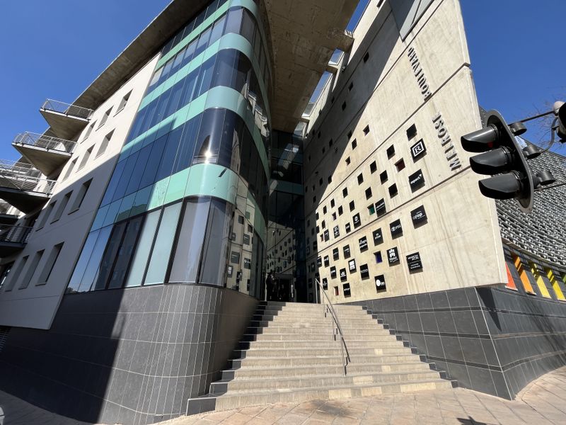 Modern commercial office building facade featuring a prominent glass curtain wall, concrete architectural elements, and a wide stone staircase entrance.