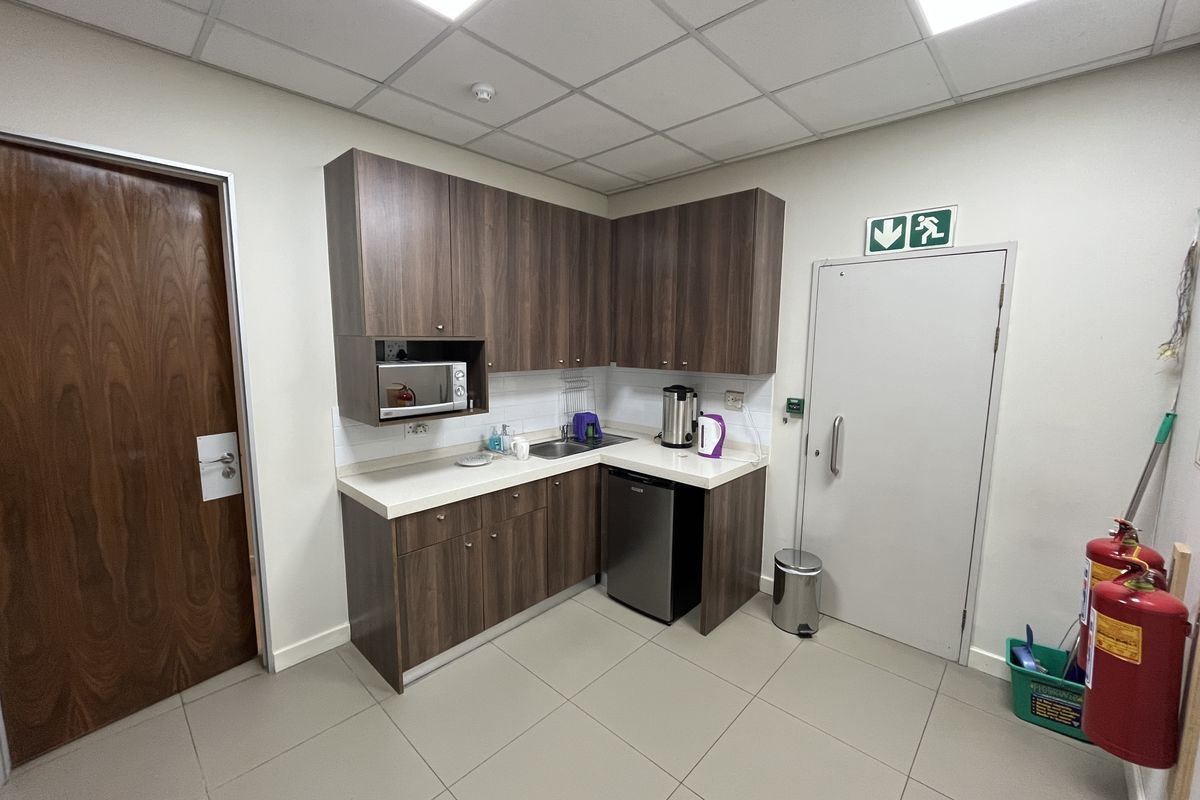 A functional office kitchenette featuring dark wood-look cabinetry, a built-in microwave, stainless steel sink, and durable tiled flooring.