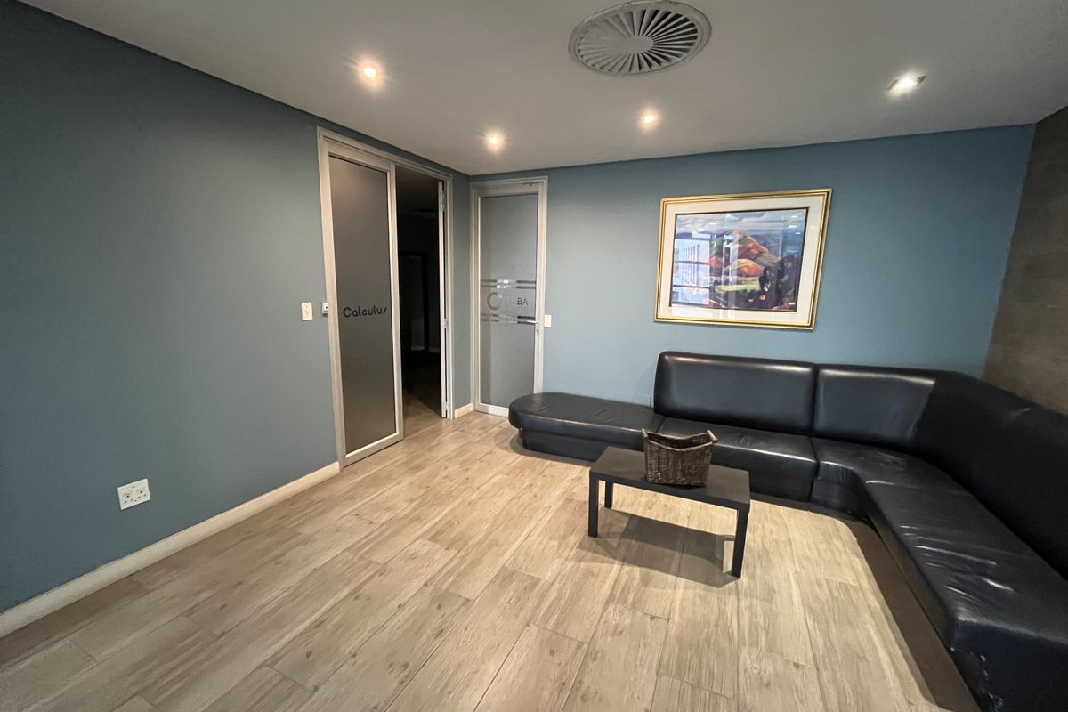 A professional office reception area featuring wood-look tile flooring, recessed lighting, and modern frosted glass entry doors.