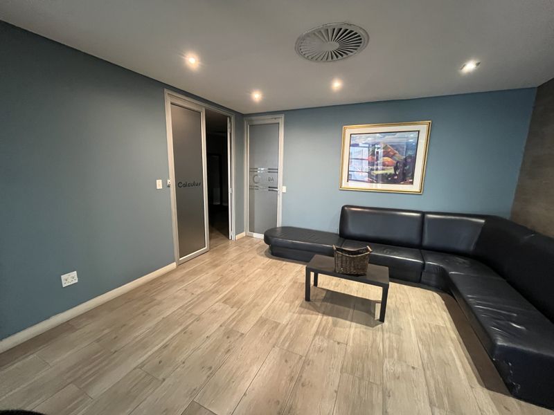 A professional office reception area featuring wood-look tile flooring, recessed lighting, and modern frosted glass entry doors.