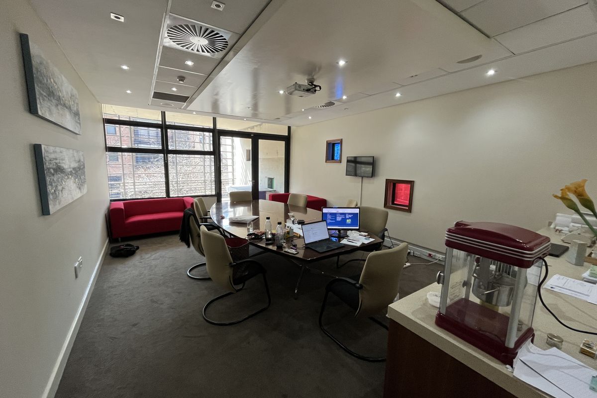 A professional office boardroom featuring recessed ceiling lighting, integrated air conditioning, a ceiling-mounted projector, and large windows providing natural light.