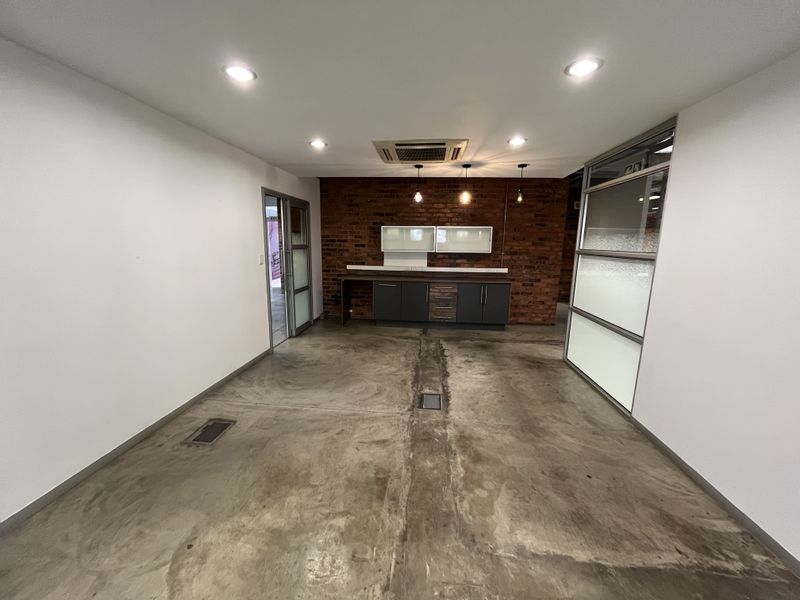 Modern office space featuring polished concrete floors, an exposed brick feature wall, integrated kitchenette cabinetry, and glass partition walls with ceiling-mounted air conditioning.