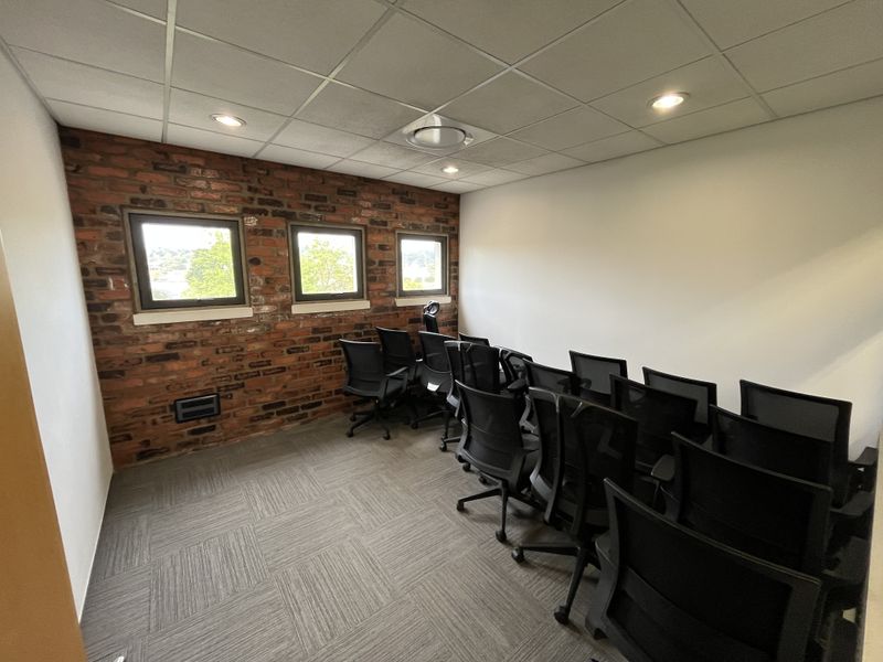 A professional office space featuring an exposed brick feature wall, suspended ceiling with recessed lighting, and durable carpet tile flooring.