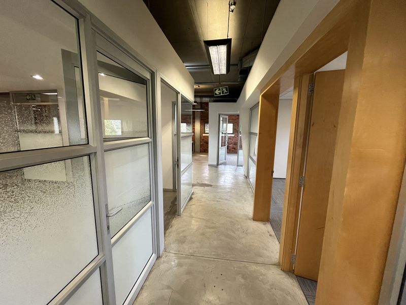 A modern industrial-style office hallway featuring polished concrete floors, glass partitions, and exposed ceilings with integrated lighting fixtures.