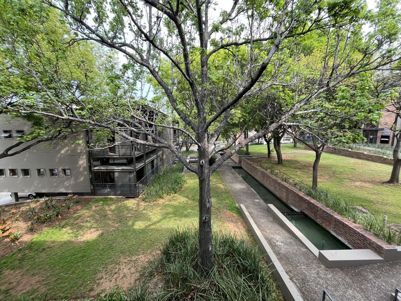 An elevated view of the office property's rear grounds, featuring landscaped gardens, a brick-lined water feature, and modern metal balcony structures.
