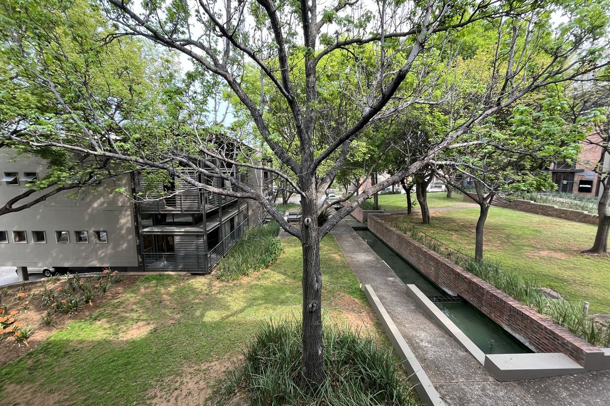 An elevated view of the office property's rear grounds, featuring landscaped gardens, a brick-lined water feature, and modern metal balcony structures.