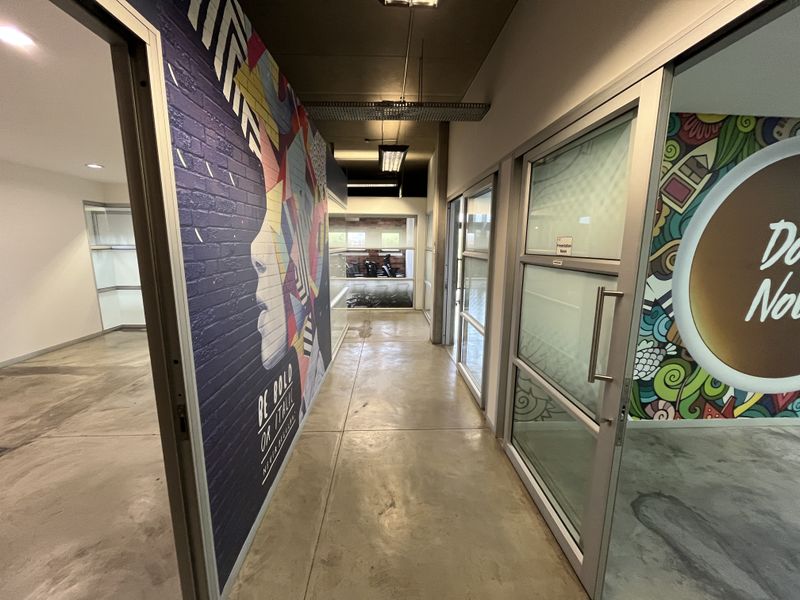 A modern office hallway featuring polished concrete floors, aluminum-framed glass office partitions, and vibrant mural wall art.